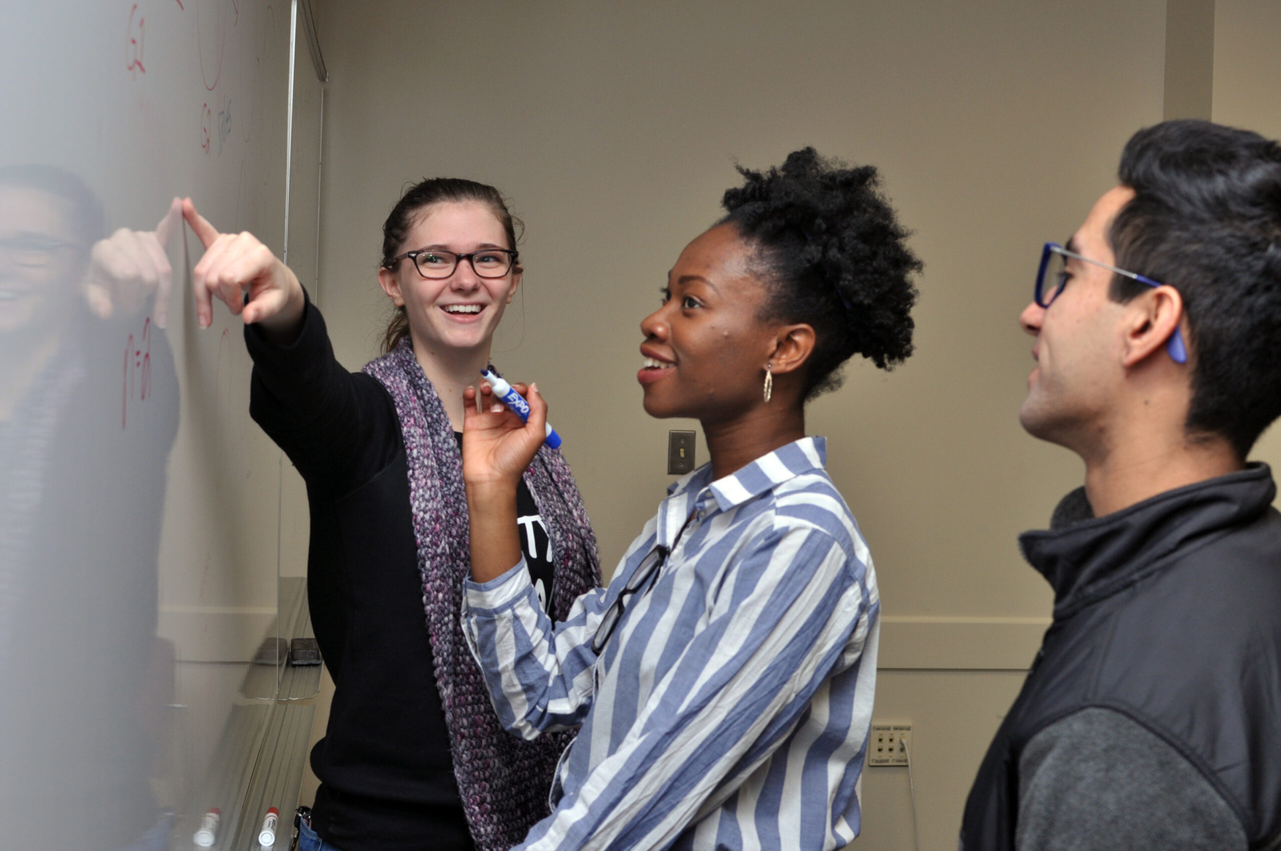 A tutor instructing two students at a white board