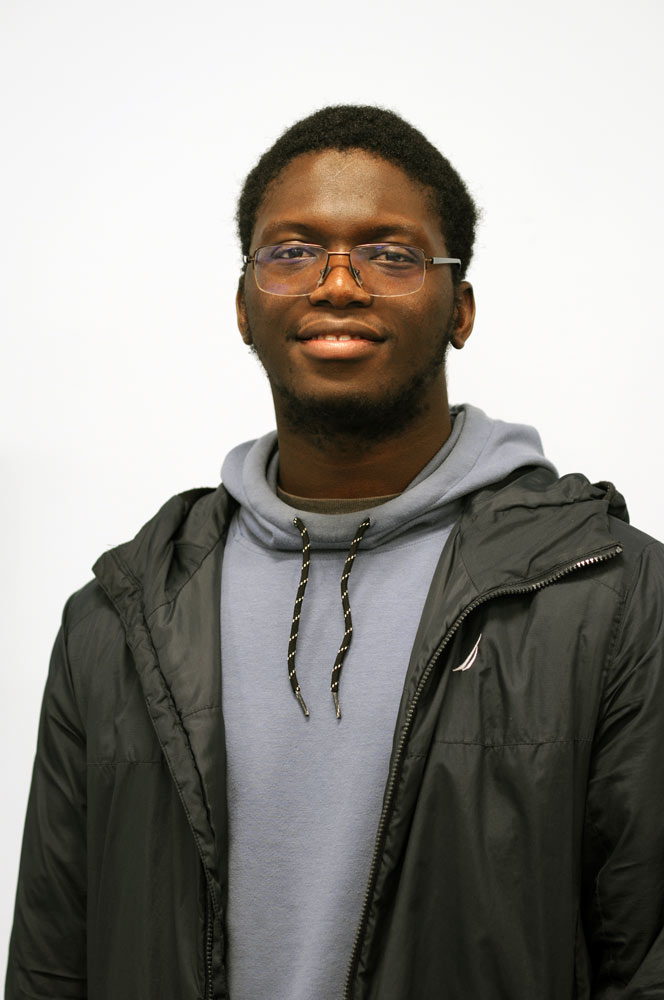 A three quarter portrait of a young man smiling in his dorm room.