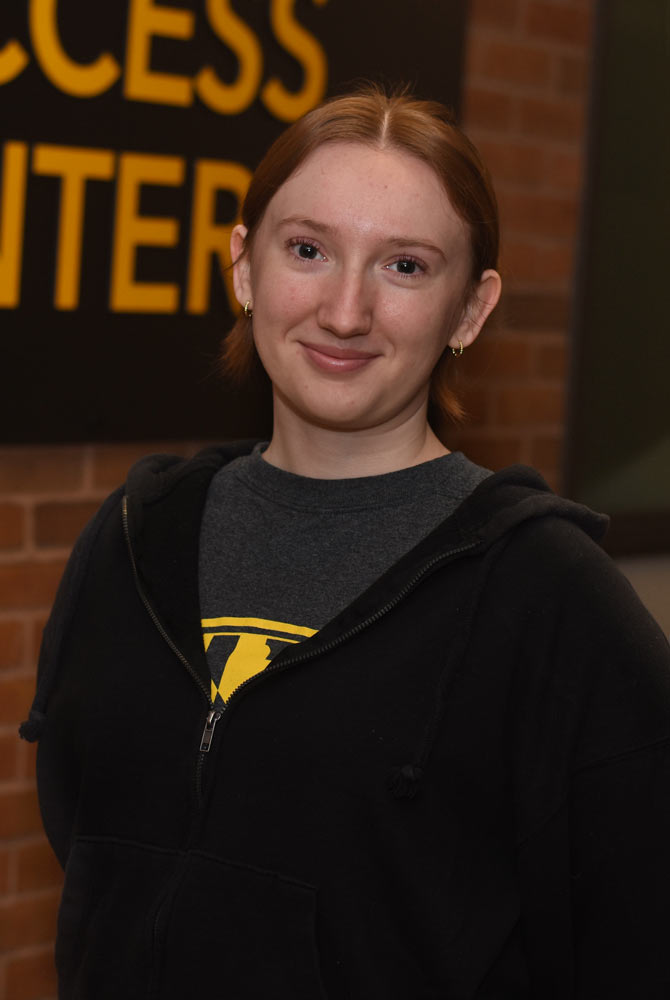 Sarah is standing in front of the academic success center's ofices, she is smiling